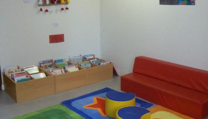 espace des enfants, tapis de couleurs et assises rouges. Bacs d'albums autour de cet espace
