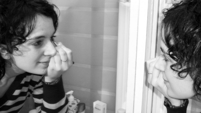 Photo noir et blanc d'une femme se maquillant devant un miroir.