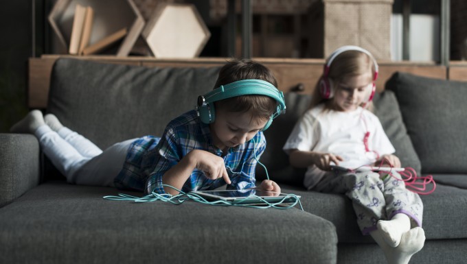 Deux enfants dans un canapé avec tablettes et casques audios