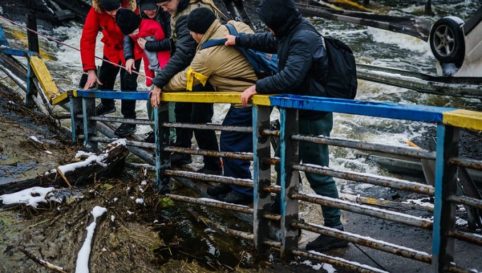 Des soldats ukrainiens aidant une famille à franchir un pont détruit à Irpin.
