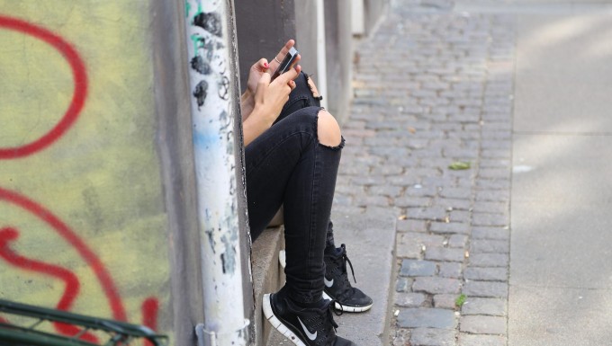 Photographie d'une adolescente utilisant son smartphone dans un milieu urbain.