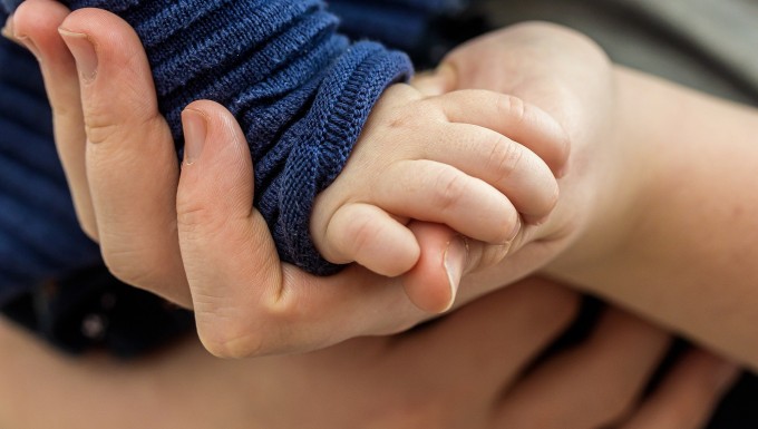 Photo en gros plan d'une main de bébé soutenue par une main d'adulte.