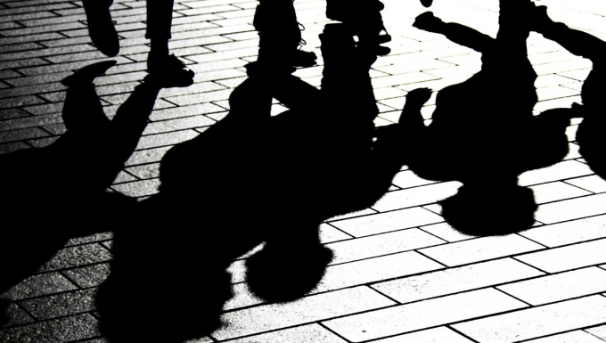 Photo en noir et blanc de personnes démabulant dont les ombres se reflétent au sol.