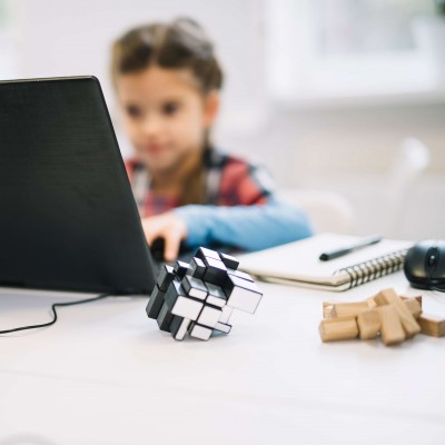 Une enfant utilisant un ordinateur portable. Au premier plan, des jeux de logique sont posés sur une table. 