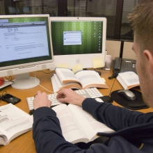 Personne photographiée de dos travaillant devant un écran d'ordinateur