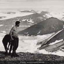 Photographie de trois personnes au sommet d'une montagne. Un homme est torse-nu. Ils ont un piolet. Ils regardent le second plan. Le sommet des montagnes enneigées.