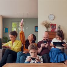 Une famille rassemblée dans son salon. Chacun des membres utilisent un appareil numérique.
