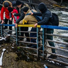 Des soldats ukrainiens aidant une famille à franchir un pont détruit à Irpin.