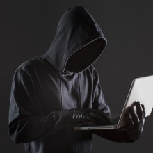 Une personne au visage dissimulé utilisant un ordinateur portable.